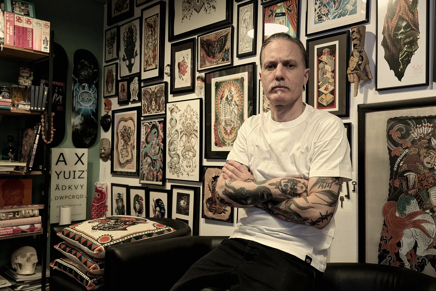 Estantería del estudio con libros de tatuaje tradicional y polinesio, junto a un rollo de flash japonés enmarcado.