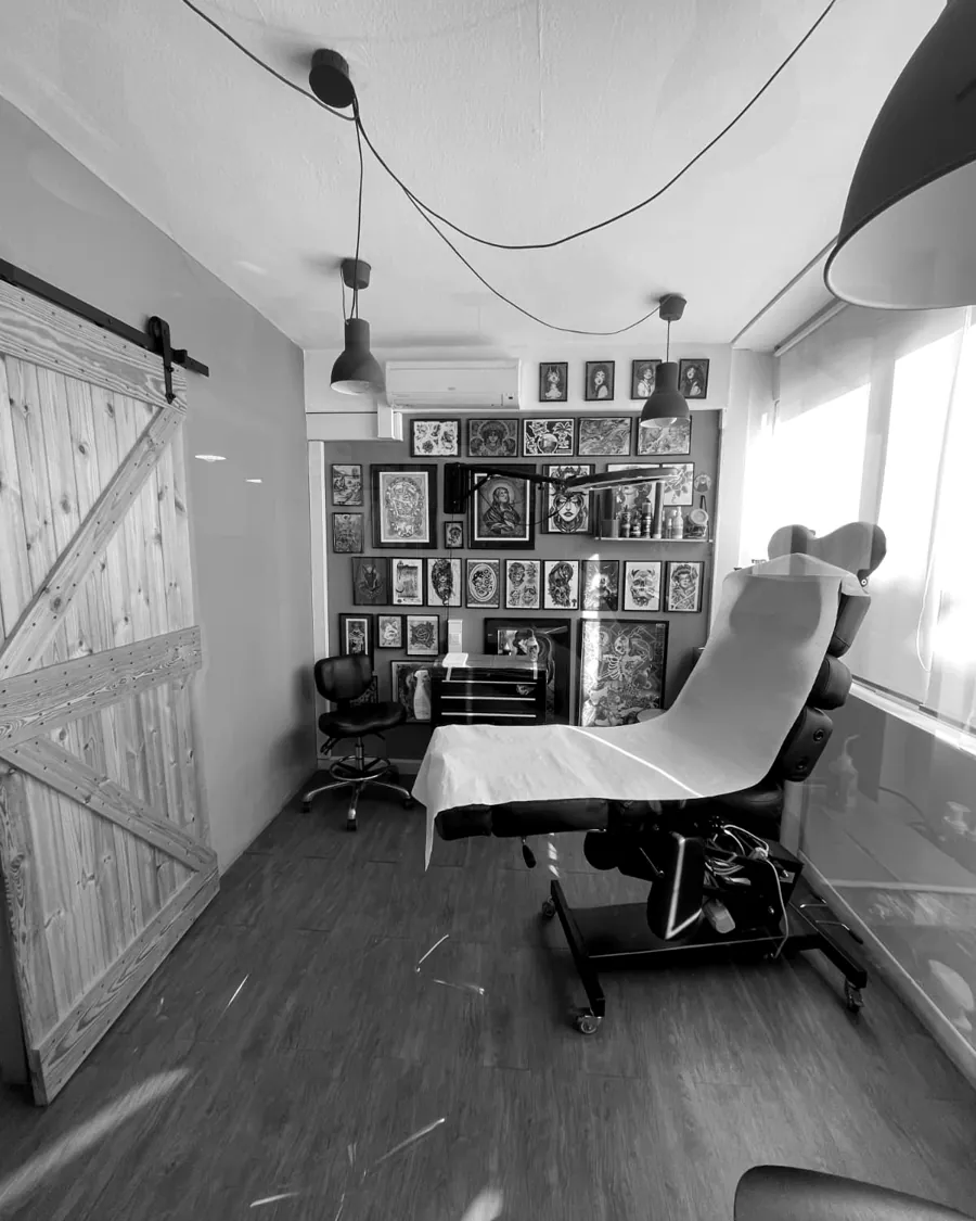 Cabina de tatuaje de A Sailor's Grave Tattoo en Granollers: camilla preparada con papel protector, puerta corredera de madera y pared de flash enmarcado.