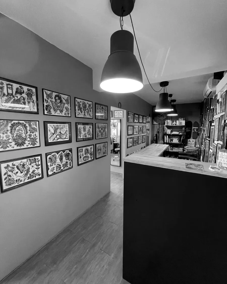Vista del pasillo de A Sailor's Grave Tattoo desde el mostrador de recepción, con las paredes cubiertas de láminas de tatuaje tradicional enmarcadas.